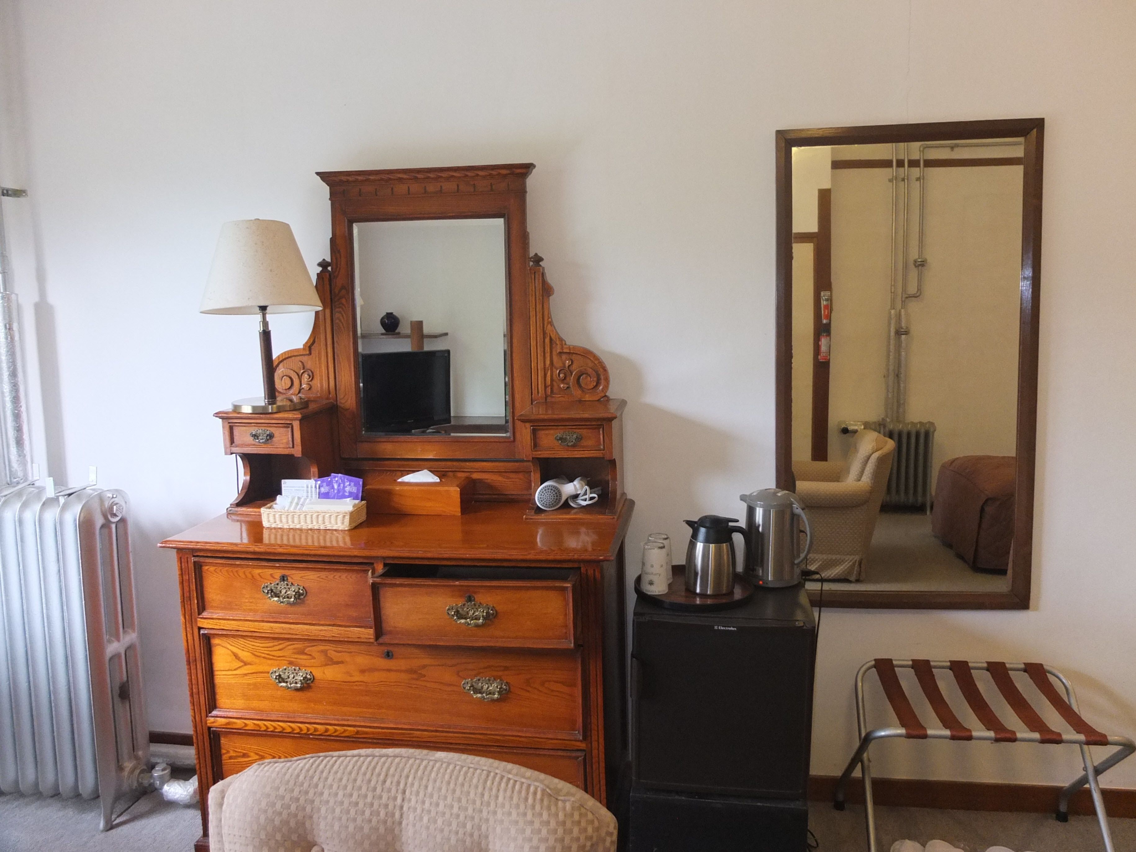 A wooden dresser with drawers, a mirror, a lamp, and a kettle.