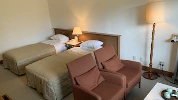 A hotel room with two single beds, a brown armchair, a small table with a tray of tea and snacks, and a bedside lamp.