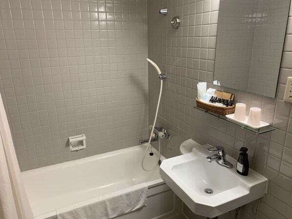 Un baño con una bañera blanca, un lavabo y una ducha. Hay un perchero y un estante con artículos de aseo.