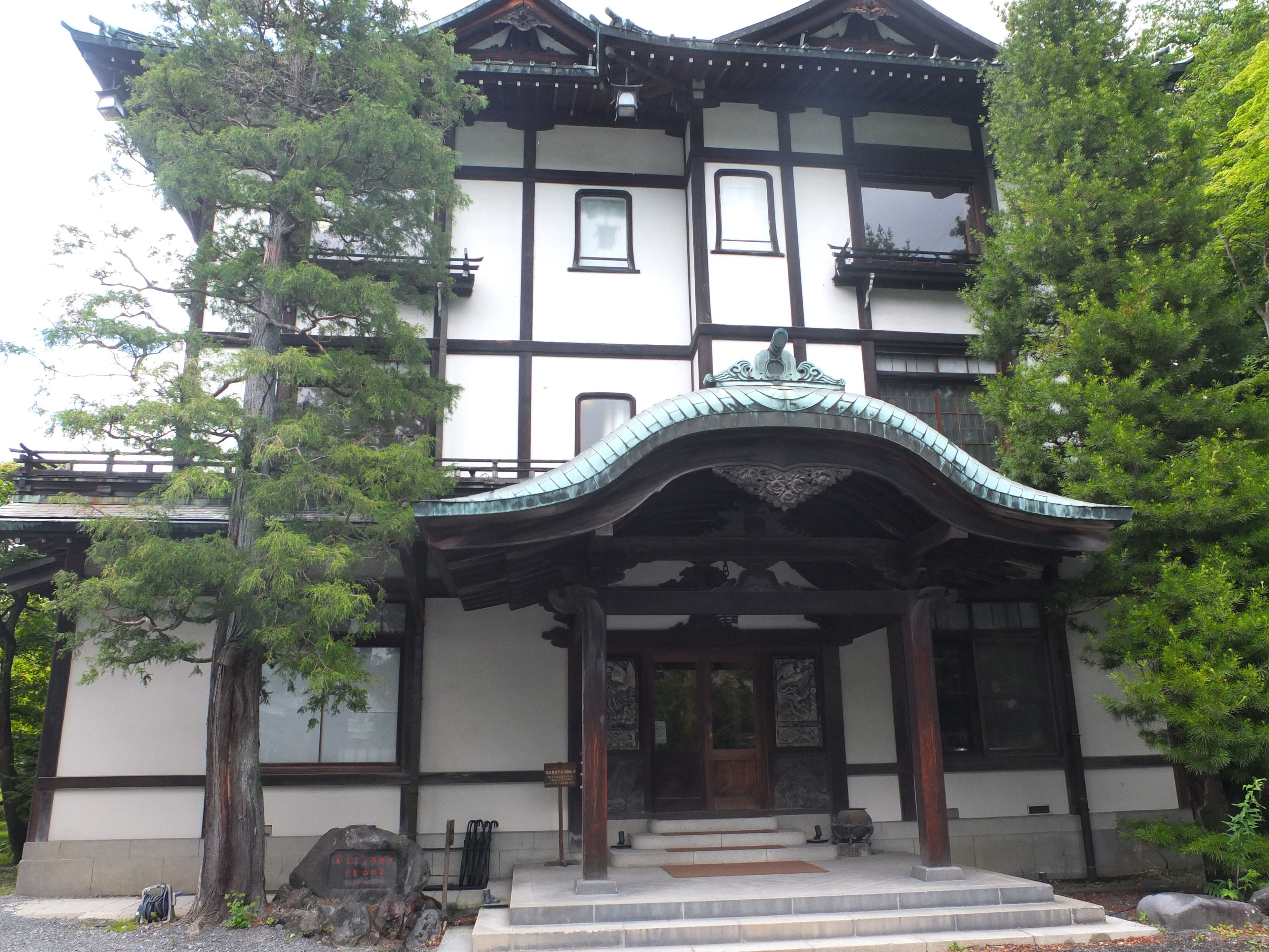 A traditional Japanese building with a curved roof, wooden beams, and a stone lantern at the entrance.