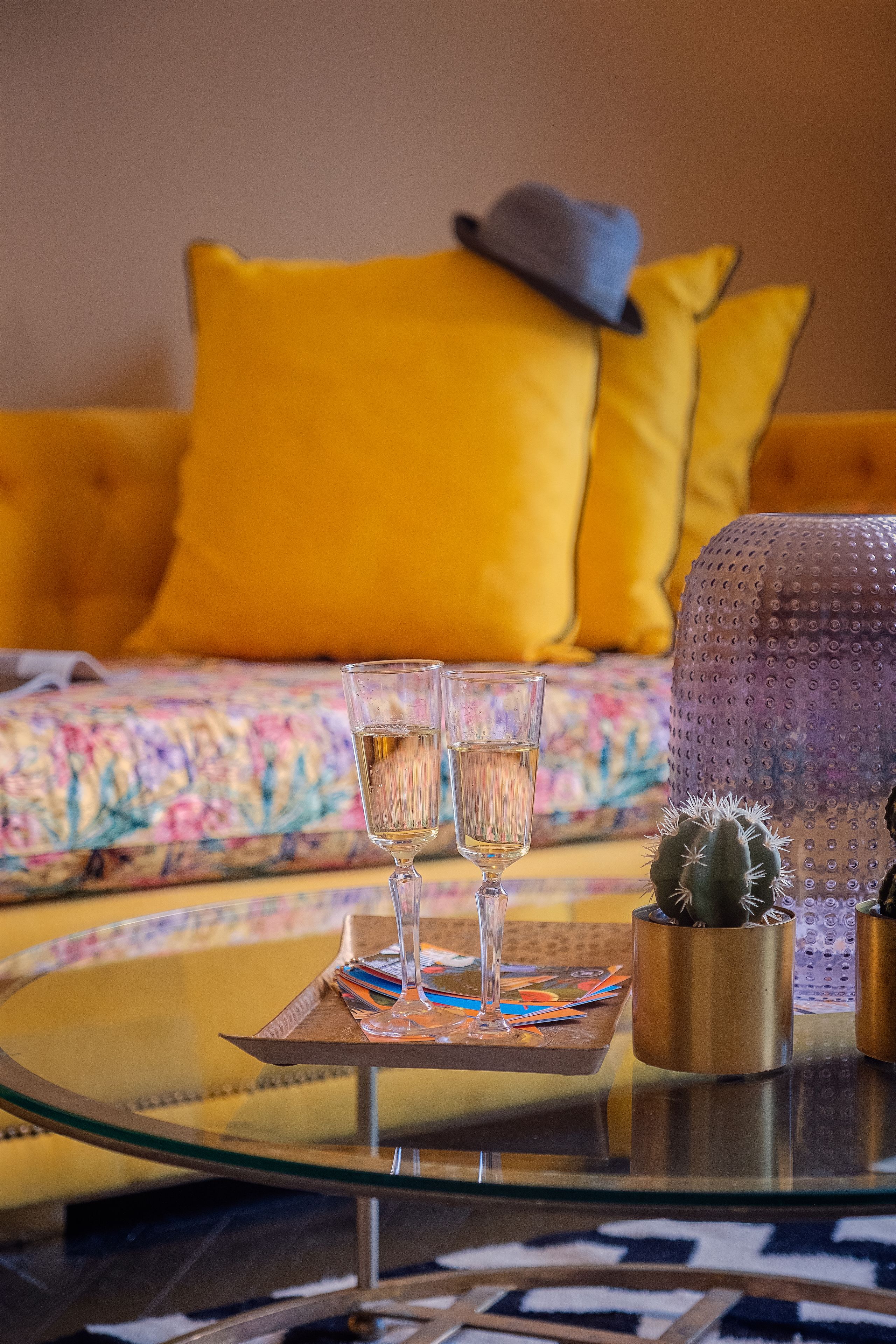 Una mesa de vidrio con dos vasos de agua, un cactus y una bandeja decorativa.