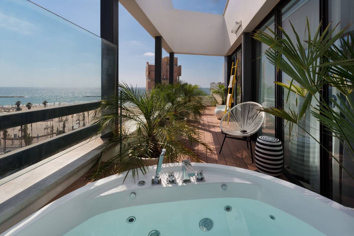 Un balcon avec un jacuzzi, une chaise et une vue sur la plage et l’océan.