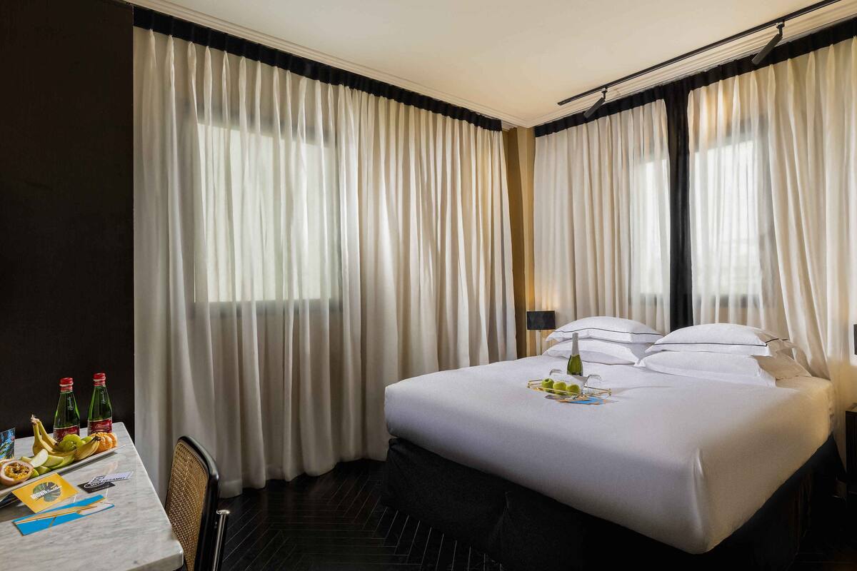 Une chambre d’hôtel avec un lit bien fait, une table avec des articles pour le petit-déjeuner et des rideaux.