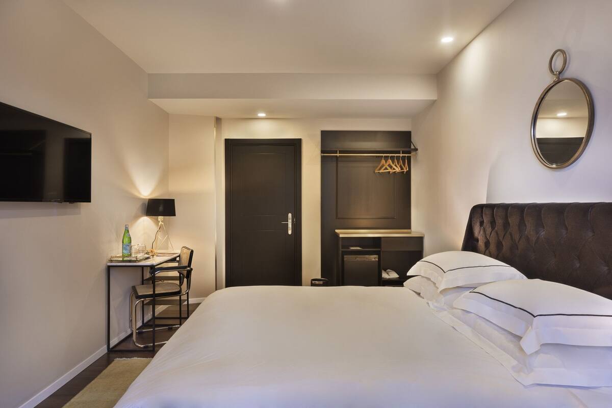 Une chambre d’hôtel avec un grand lit, un bureau avec une lampe, une télévision, une armoire et un miroir au mur.