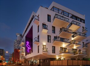 Een modern meerlaags hotel met balkons, een neonbord en uitzicht op de straat.