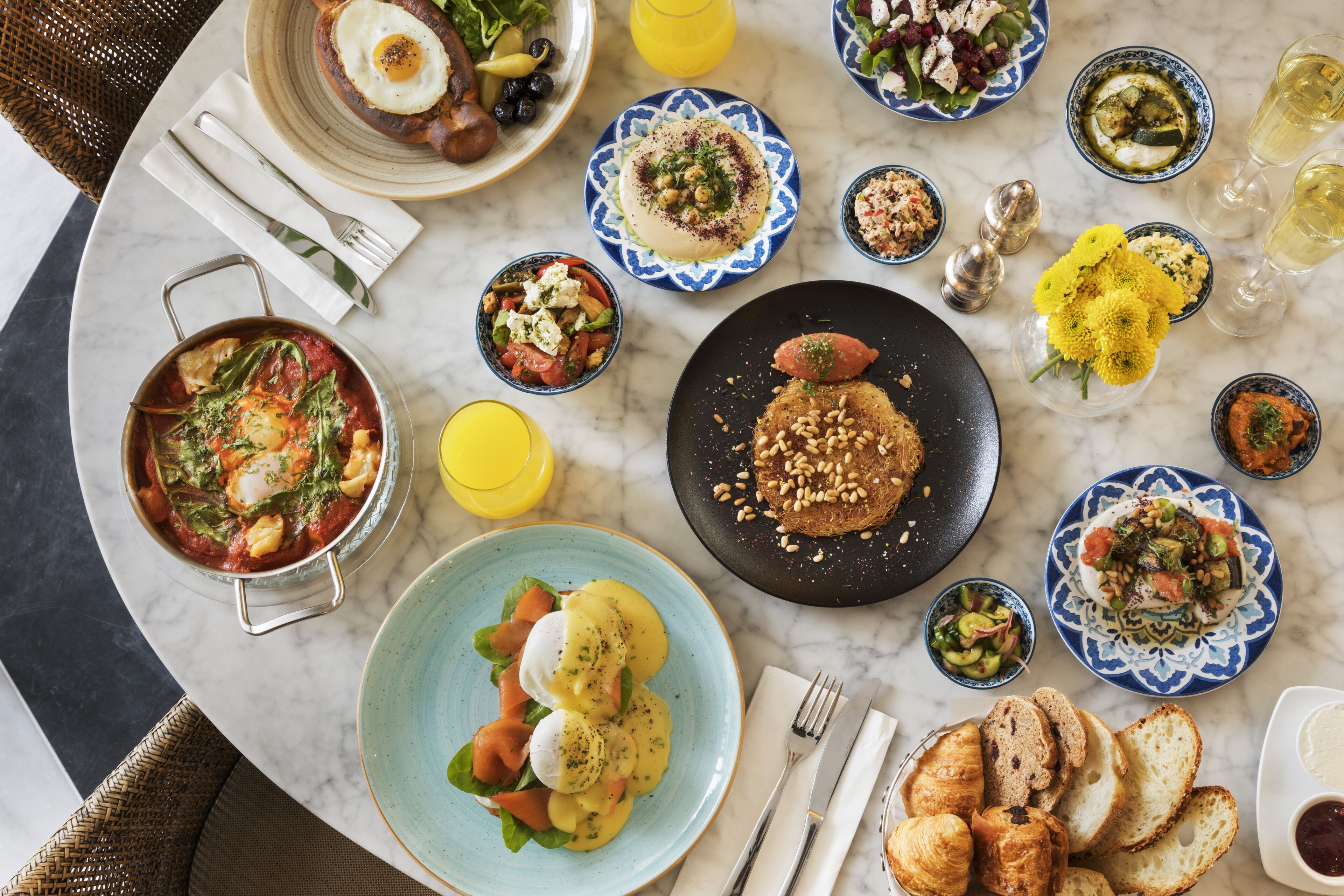 A variety of dishes on a marble table, including a bowl of soup, a plate of eggs benedict, and several small bowls of salad.
