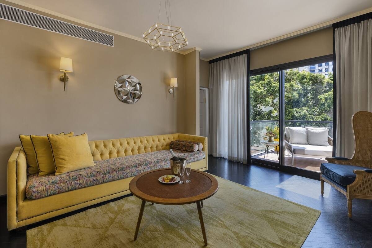 Un salon moderne avec un canapé jaune, une table basse ronde et une vue sur l’extérieur grâce à de grandes fenêtres.