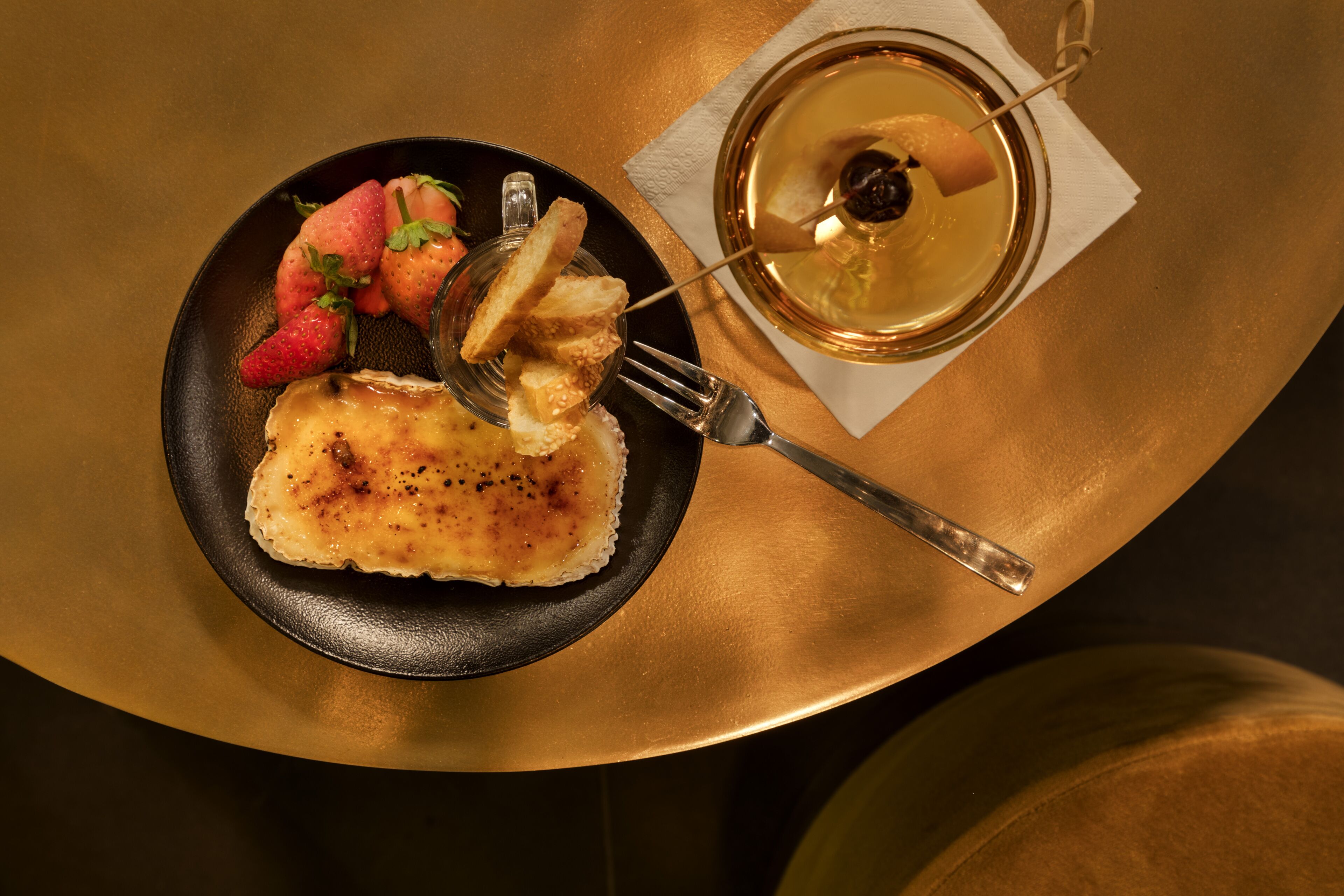 A dessert plate with a slice of cake, strawberries, and a glass of dessert wine on a table.