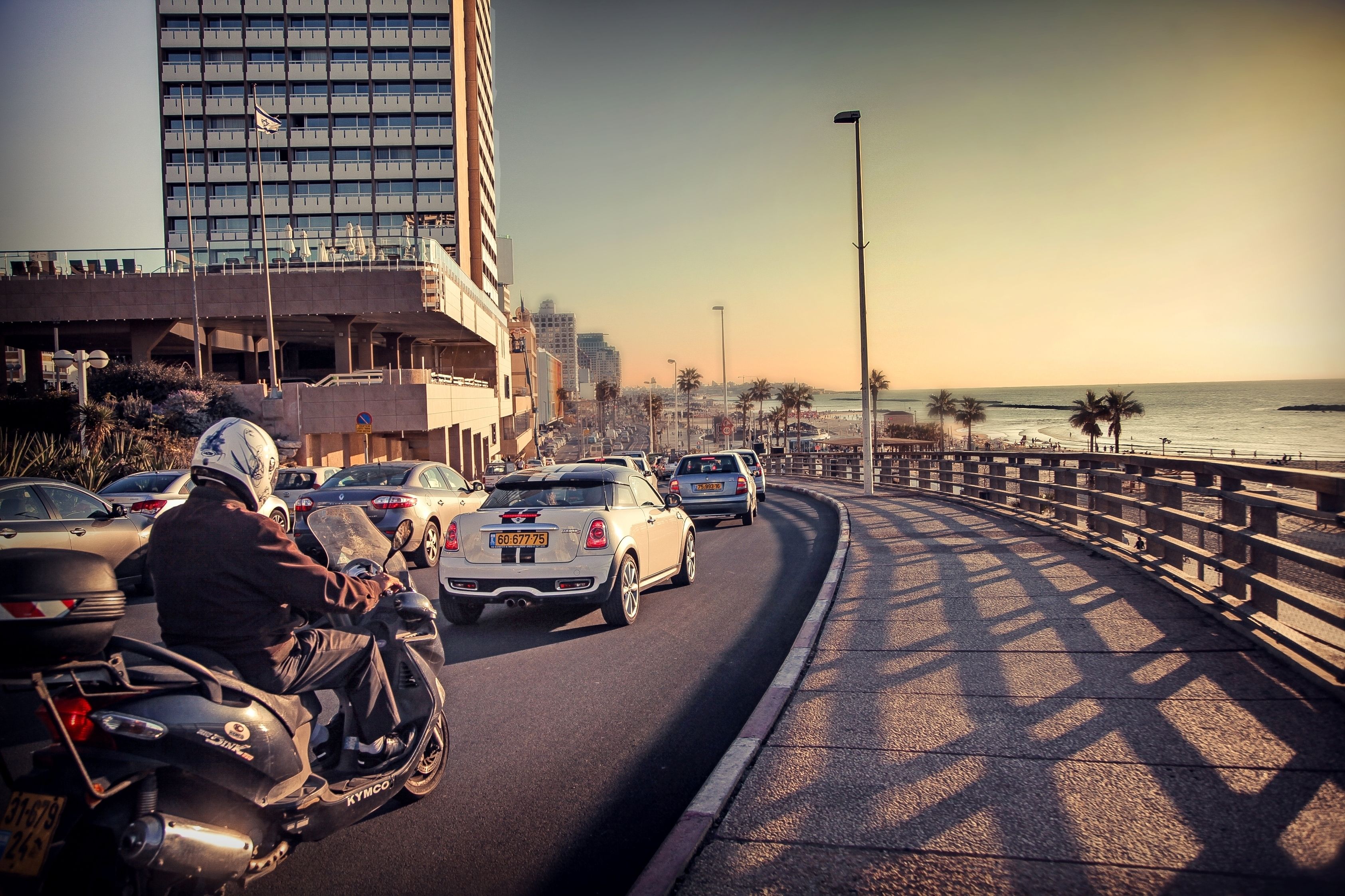 A busy coastal road with vehicles, a bridge, and a beach in the background.