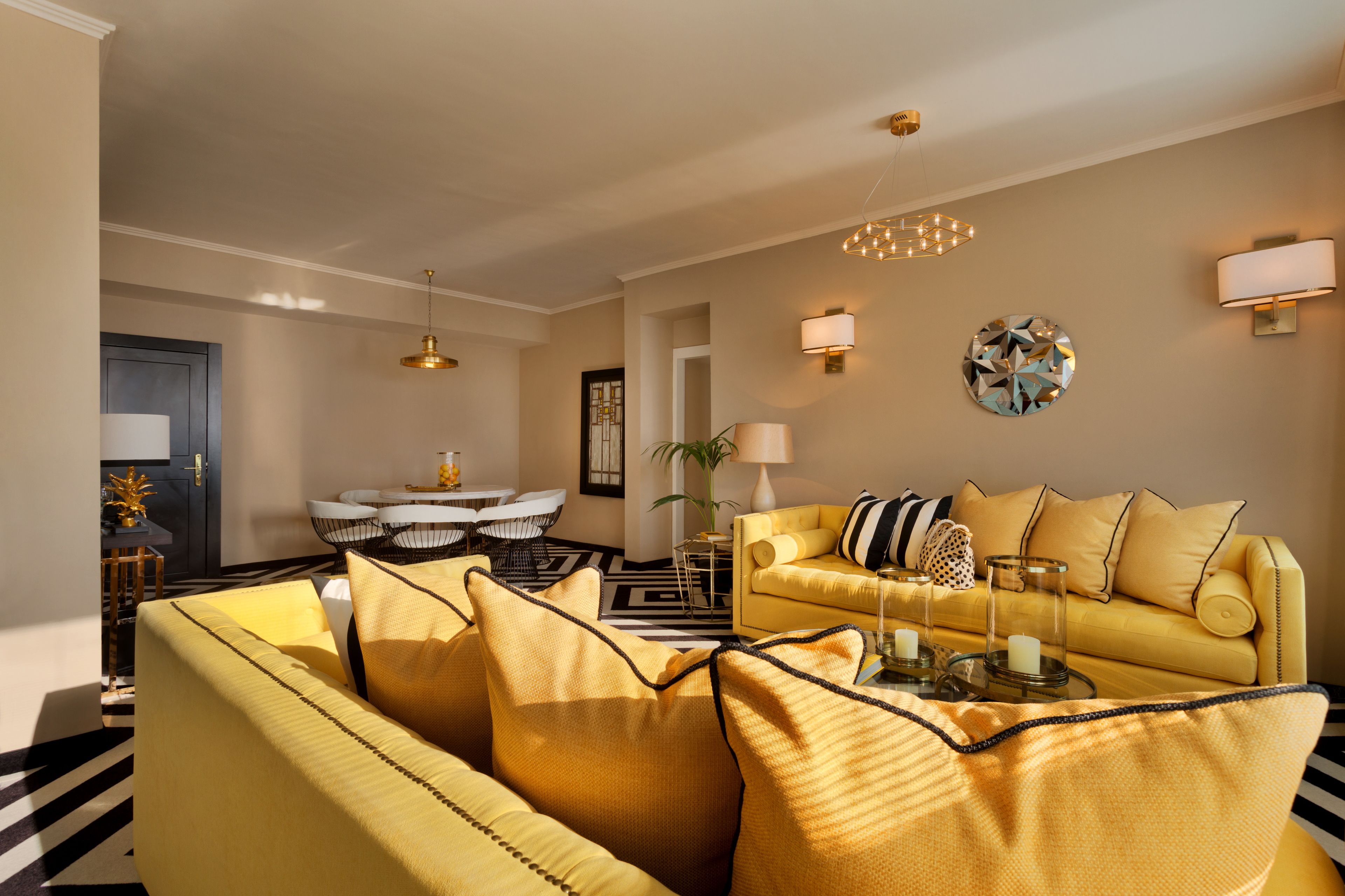 Ein Wohnzimmer mit gelben Sofas, ein Essbereich mit einem schwarz-weißen Tisch und einer Chandelier.