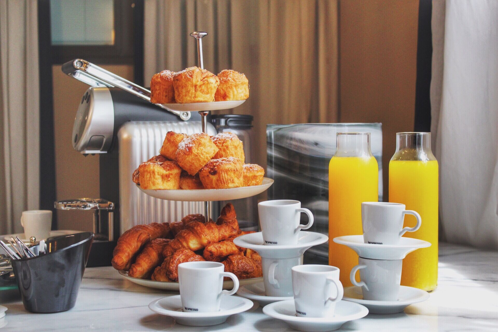 A breakfast setup with pastries, coffee cups, and orange juice bottles.