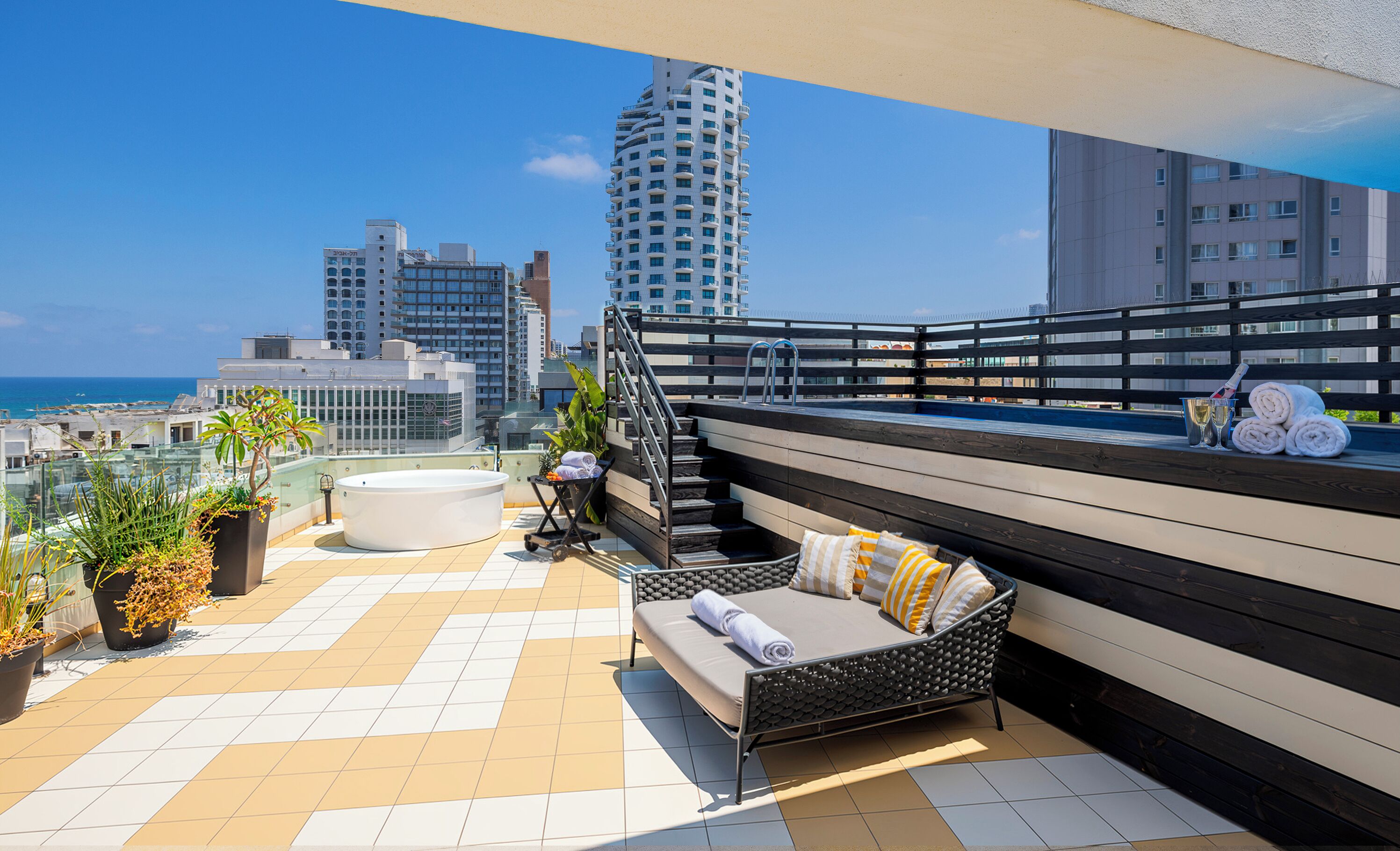 A rooftop terrace with a sofa, a hot tub, and a view of the cityscape and ocean.