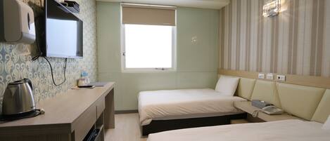 Habitación de hotel con dos camas, un escritorio con hervidor, televisor y ventana con persiana color crema.