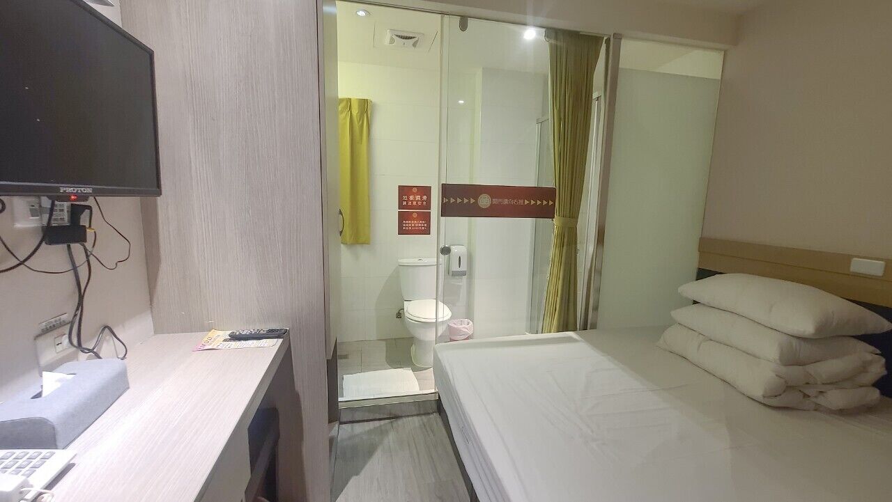 Habitación de hotel con escritorio, cama, televisor, inodoro y zona de ducha.