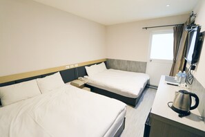 Une chambre d’hôtel avec deux lits, un bureau avec une bouilloire, une télévision et une fenêtre avec des rideaux.