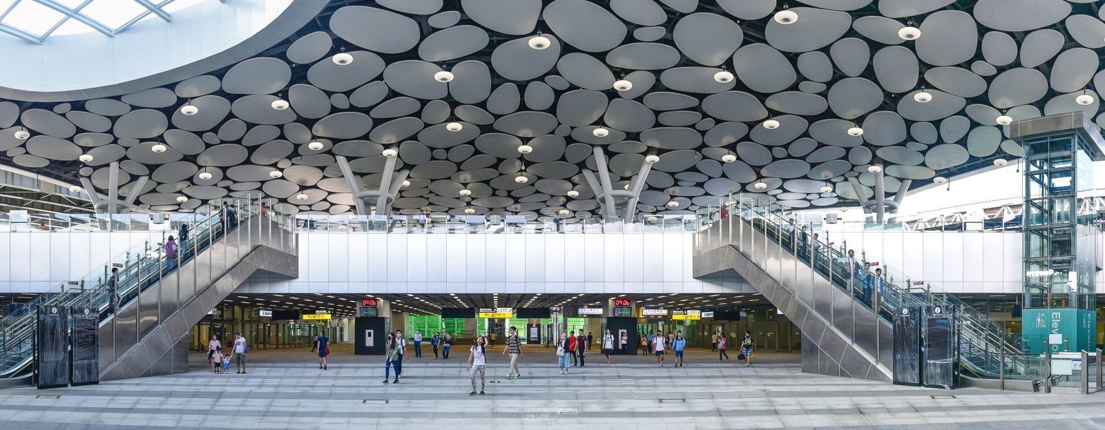 A spacious indoor area with a unique ceiling design, multiple staircases, and a central open space with people walking.