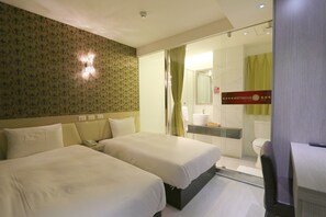 Une chambre d’hôtel avec deux lits, une salle de bain dotée d’une douche en verre et une petite table avec une chaise.