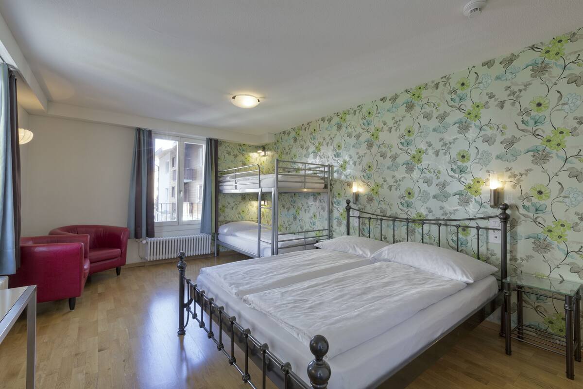 A room with two bunk beds, a red chair, a small table, and a radiator.
