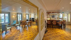 Un hall d’hôtel spacieux, doté d’un parquet en bois, de coins salons confortables et d’un bar avec des tabourets.
