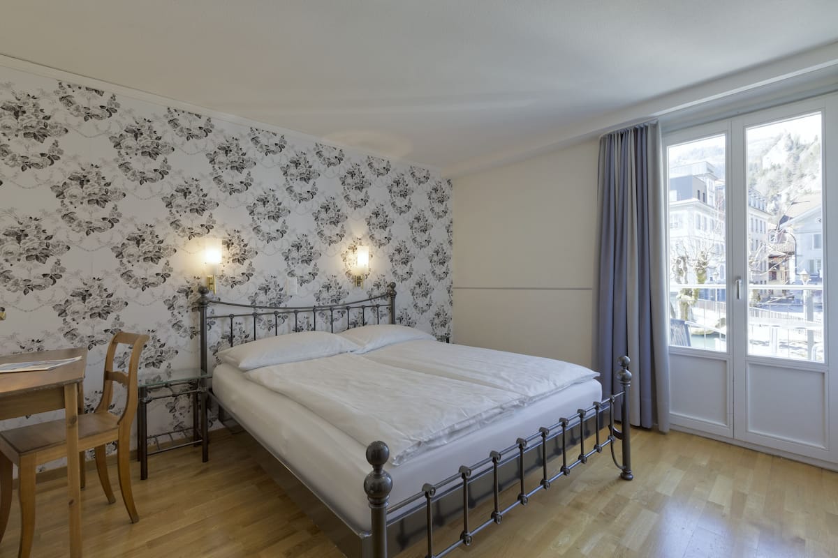 A bedroom with a bed, a desk, and a chair. There is a window with curtains.