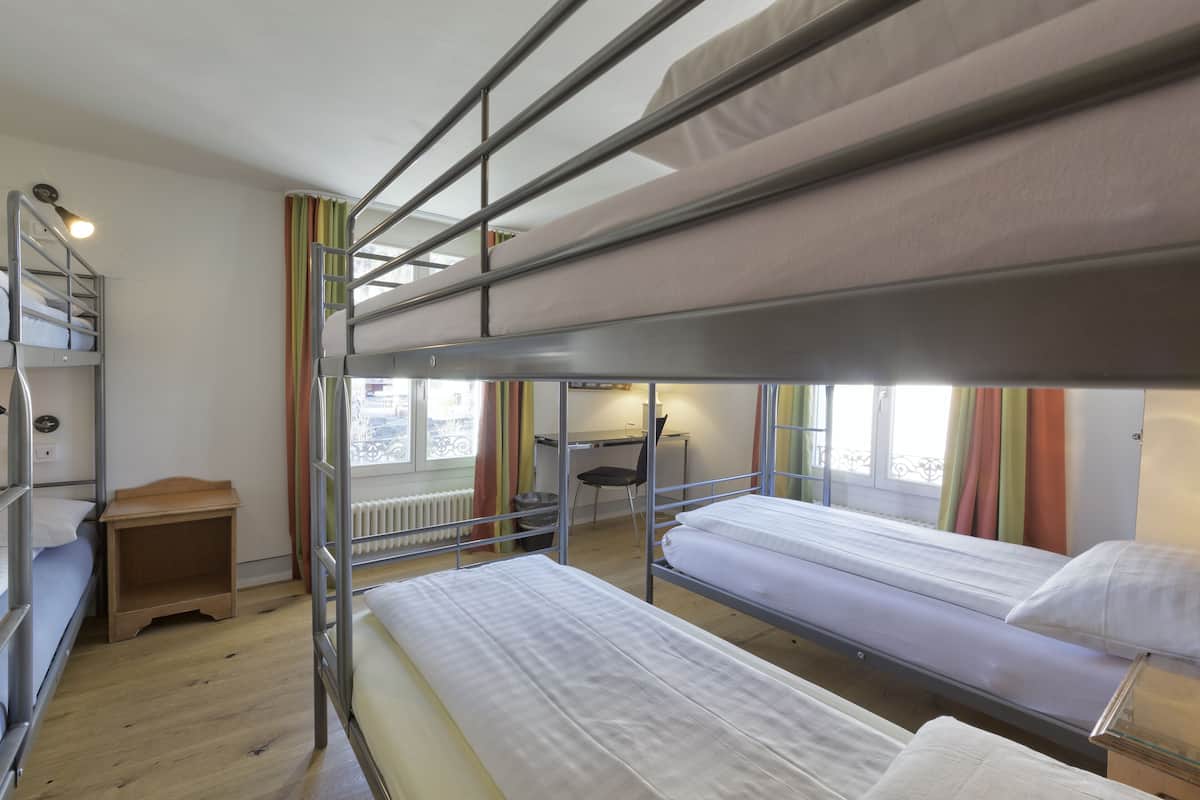 A bunk bed room with a desk and chair, a radiator, and a window with curtains.