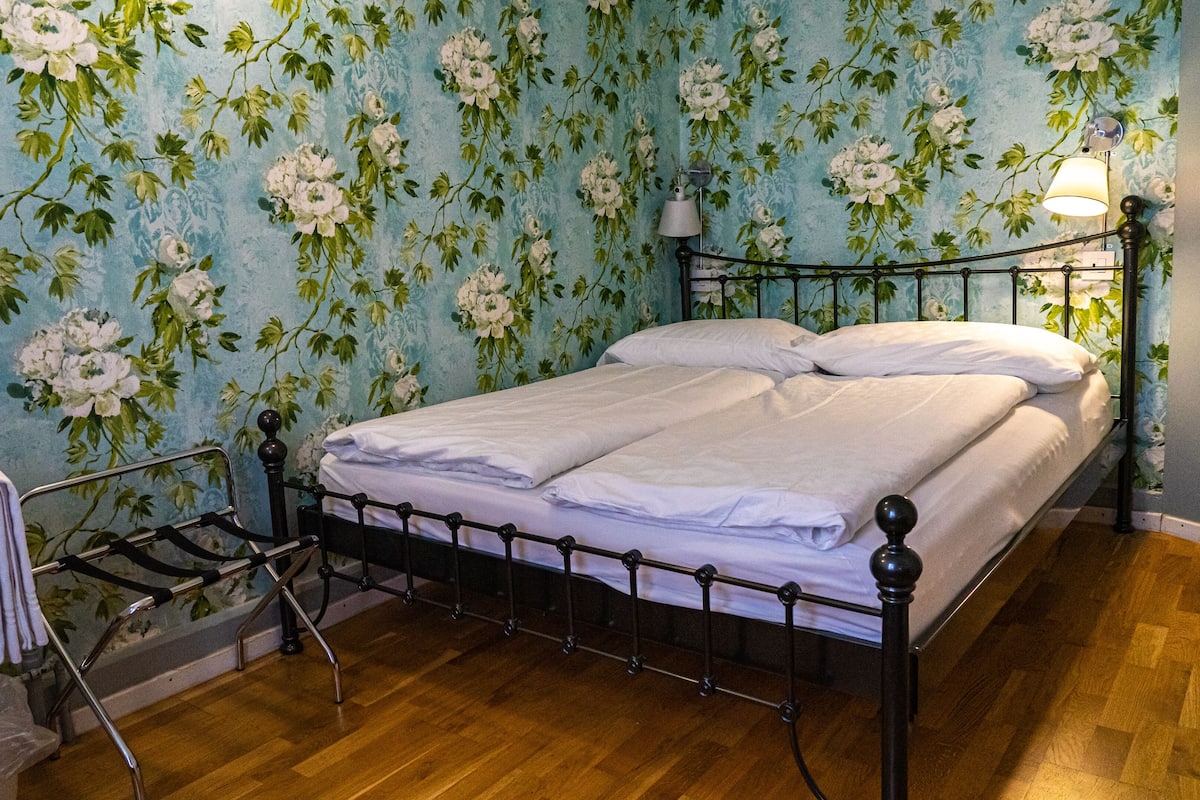 A bedroom with a bed, a nightstand, a lamp, and a wooden floor.