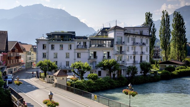 Un hôtel situé au bord de la rivière, doté de nombreux balcons, offrant une vue sur le fleuve et ayant une chaîne de montagnes en toile de fond.