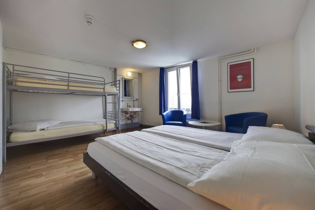 A hotel room with bunk beds, a desk, a chair, and a window with curtains.