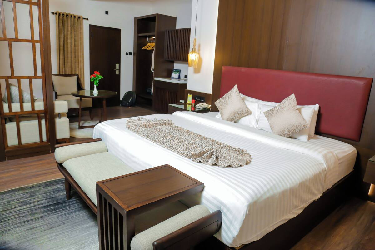 A hotel room with a large bed, a wooden headboard, a small table, a chair, a desk, and a wardrobe.