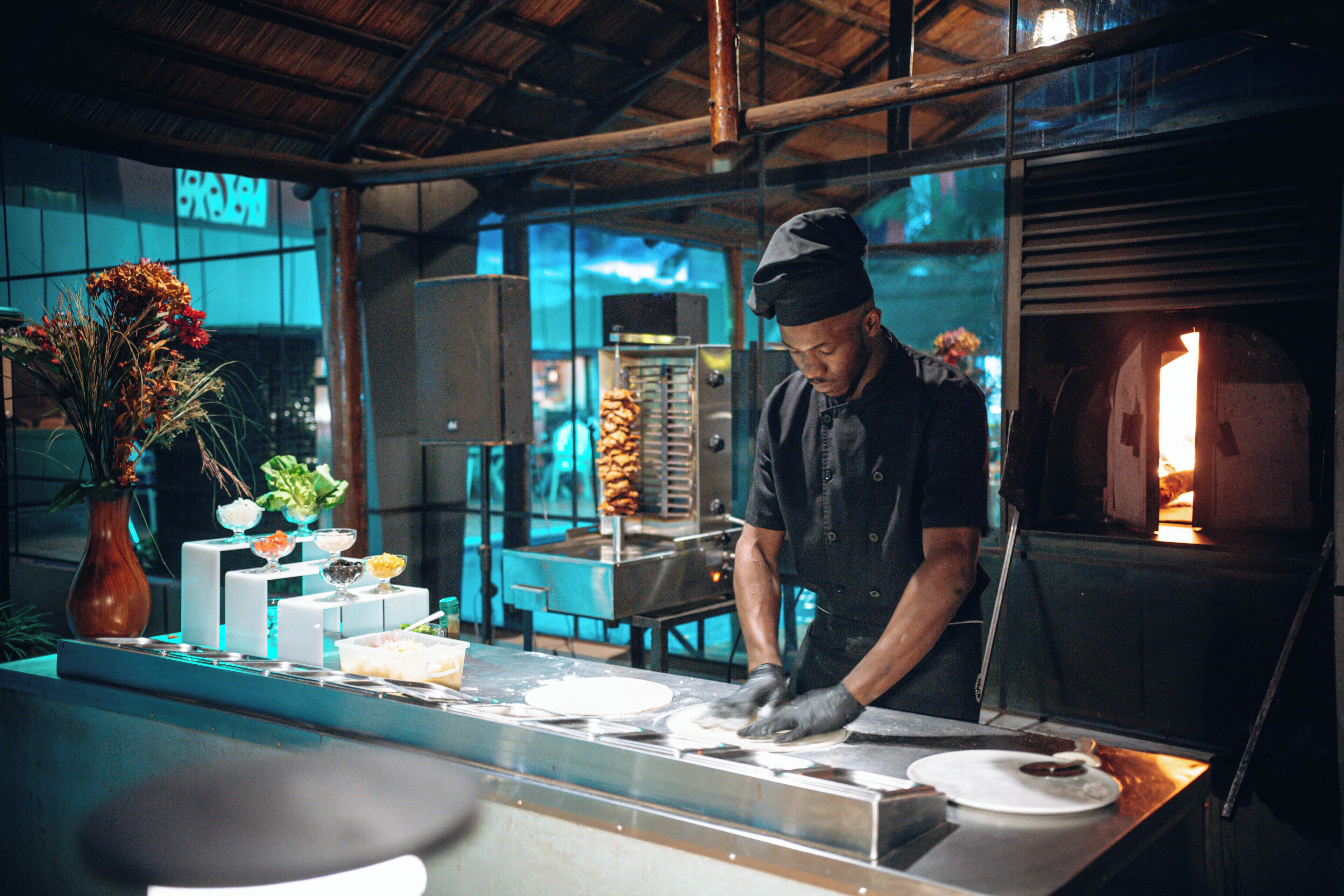 A chef preparing food at a counter with a pizza oven in the background.