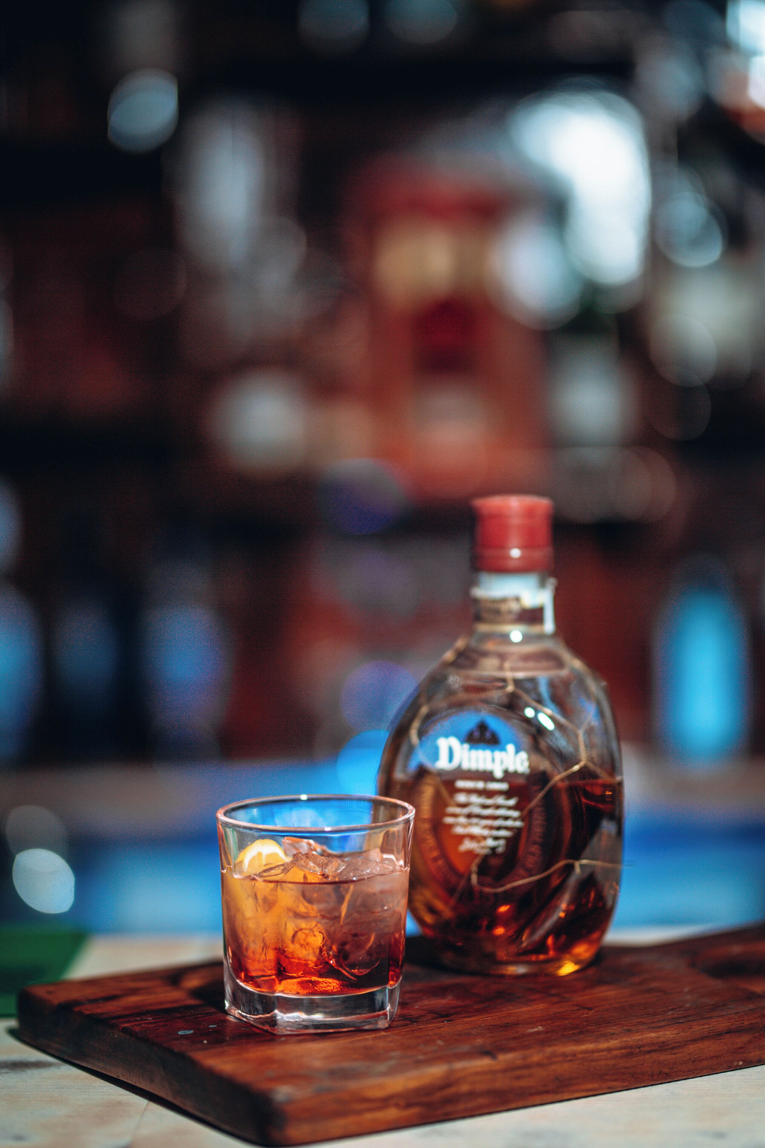 A bottle of Double Rye whiskey and a glass with ice cubes on a wooden tray.