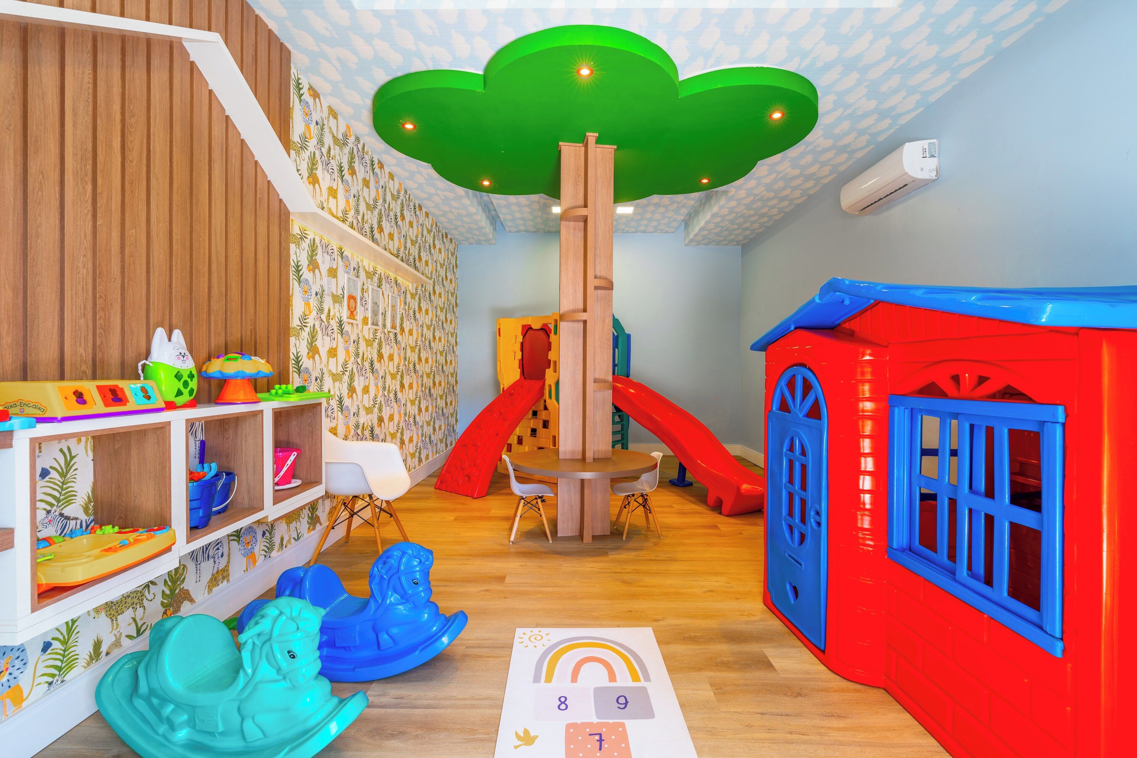 A children's playroom with a wooden floor, a playhouse, a slide, and a table with chairs.