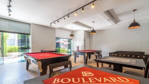 Un espace dédié aux jeux de billard, avec une table de billard recouverte d’une nappe rouge, ainsi qu’une table de baby-foot.