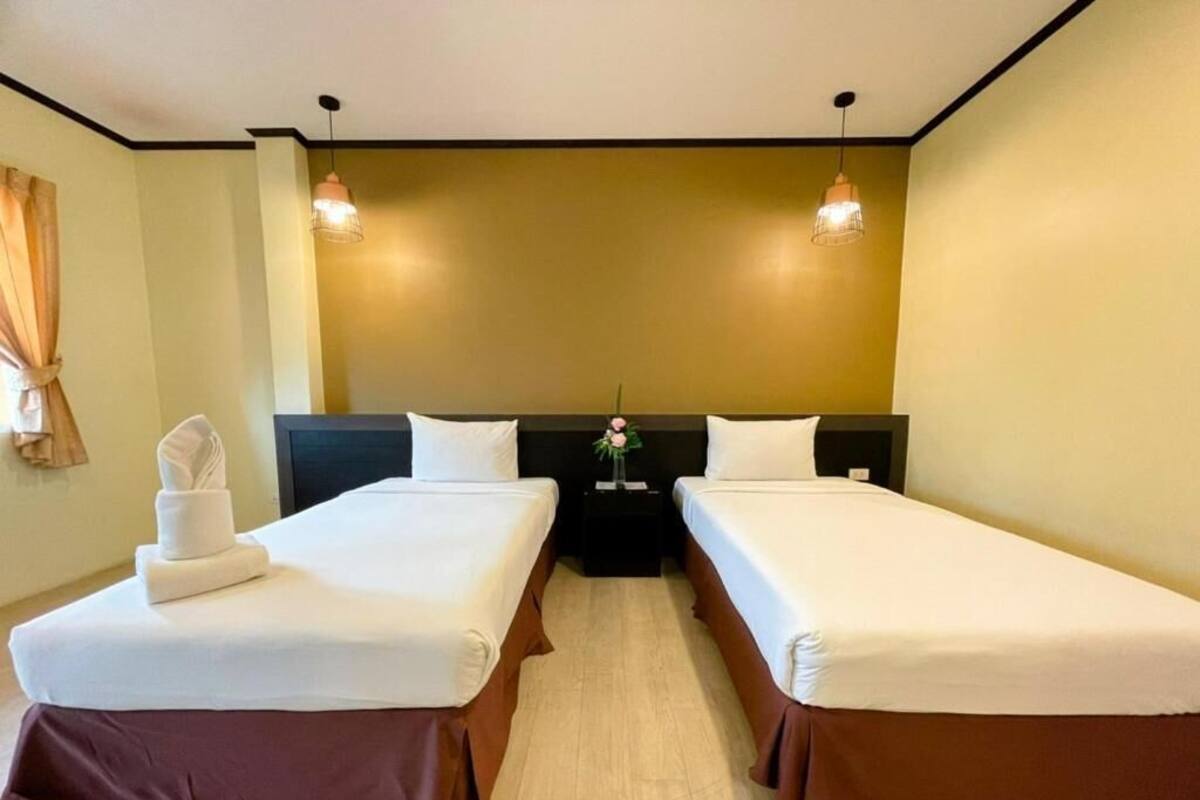 A hotel room with two single beds, a nightstand, and a wall-mounted lamp.