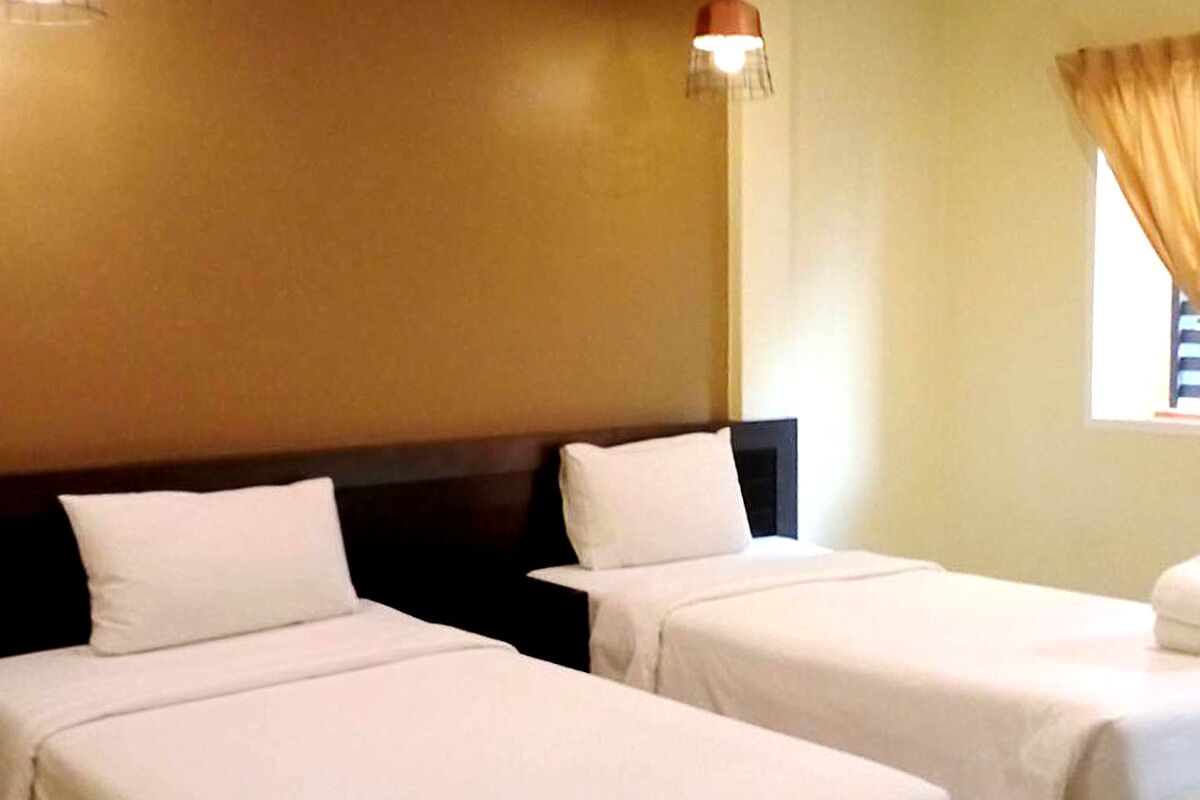 A hotel room with two beds, a headboard, a window with curtains, and a wall-mounted lamp.