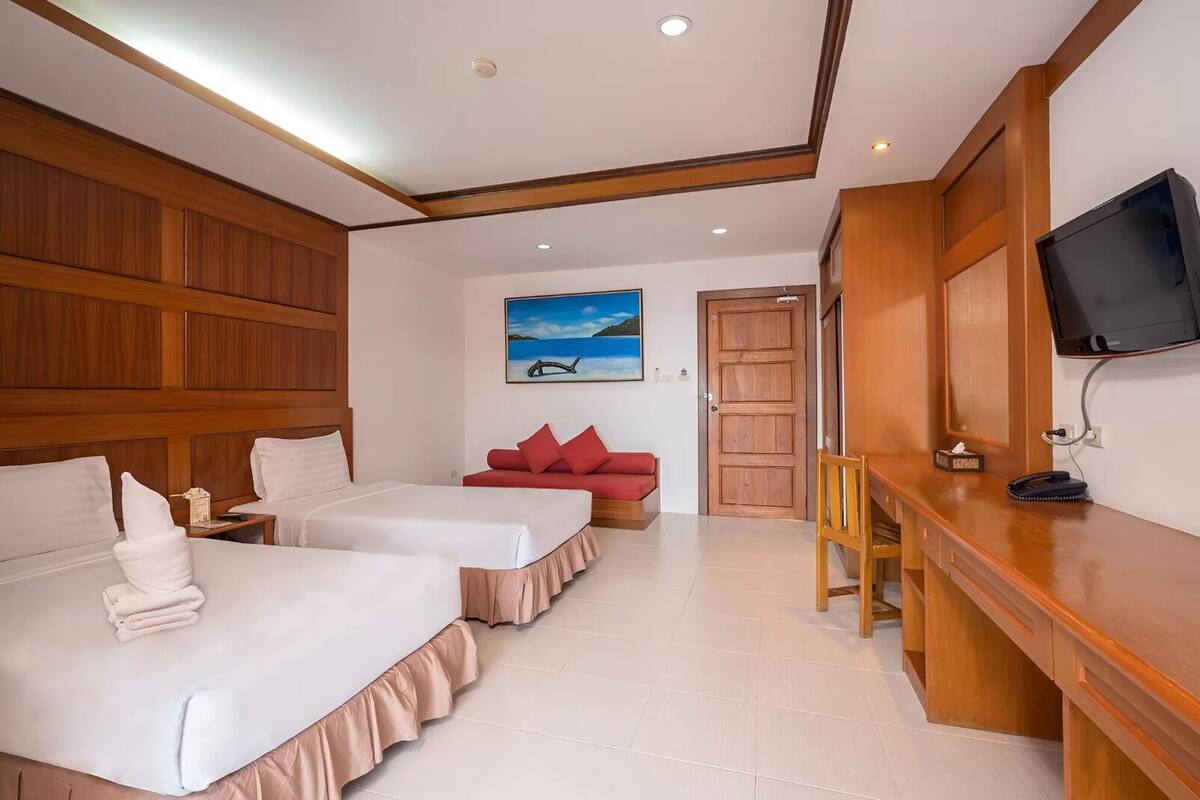 A hotel room with two beds, a red sofa, a desk with a TV, and a painting of a beach scene.