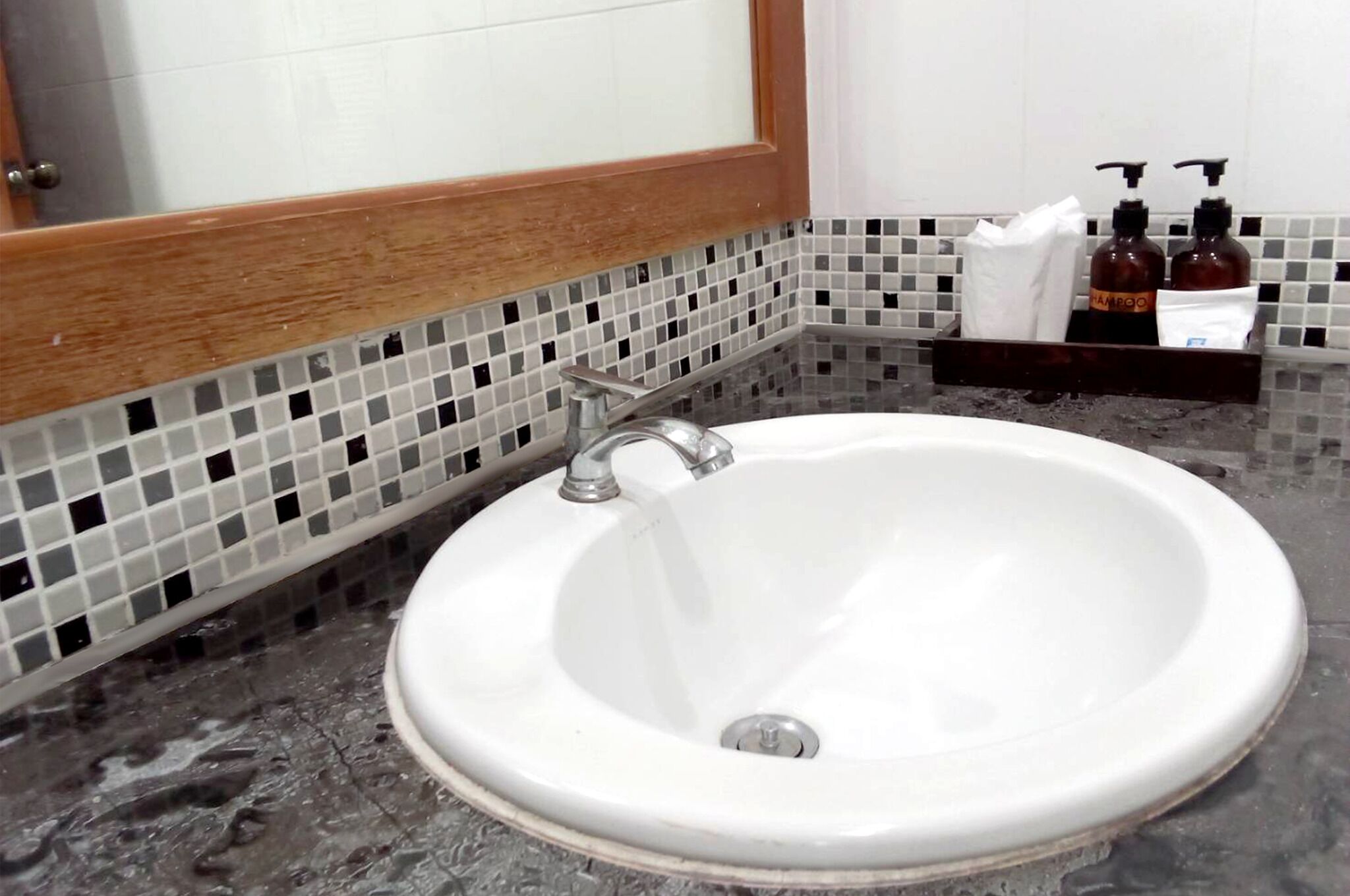 Une salle de bain avec un lavabo blanc, un miroir et un mur recouvert de carreaux.