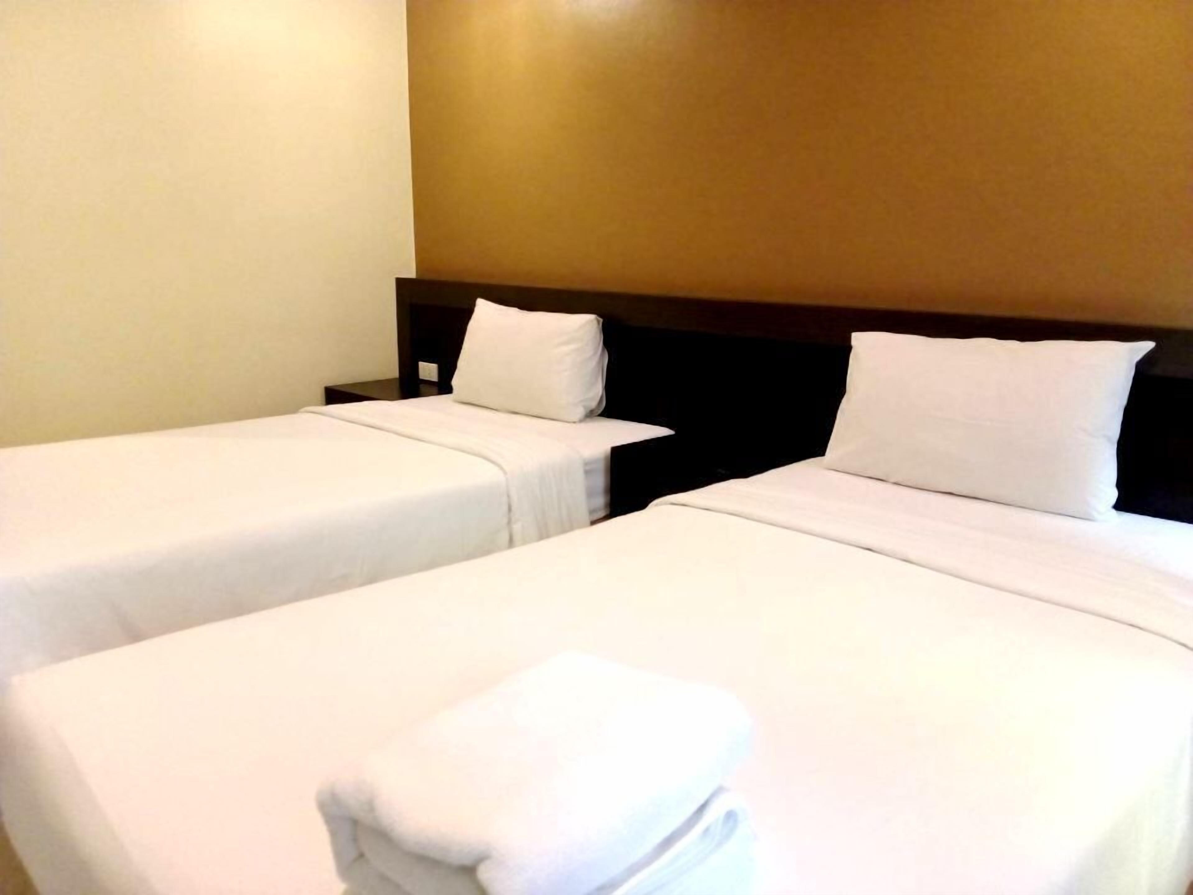 A hotel room with two single beds, each with white linens and pillows, and a neatly folded white towel on the bed.