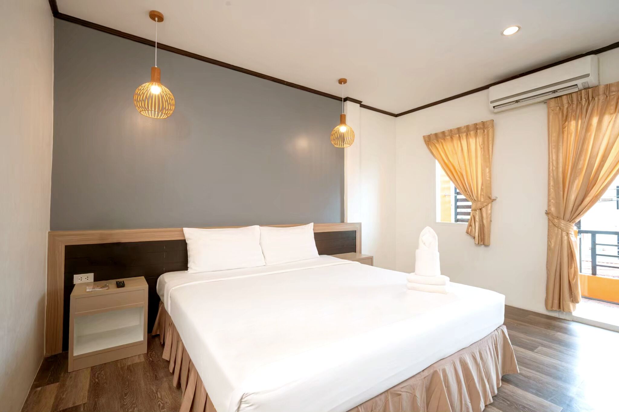 A modern hotel room with a large bed, two pendant lights, a nightstand, and a window with curtains.