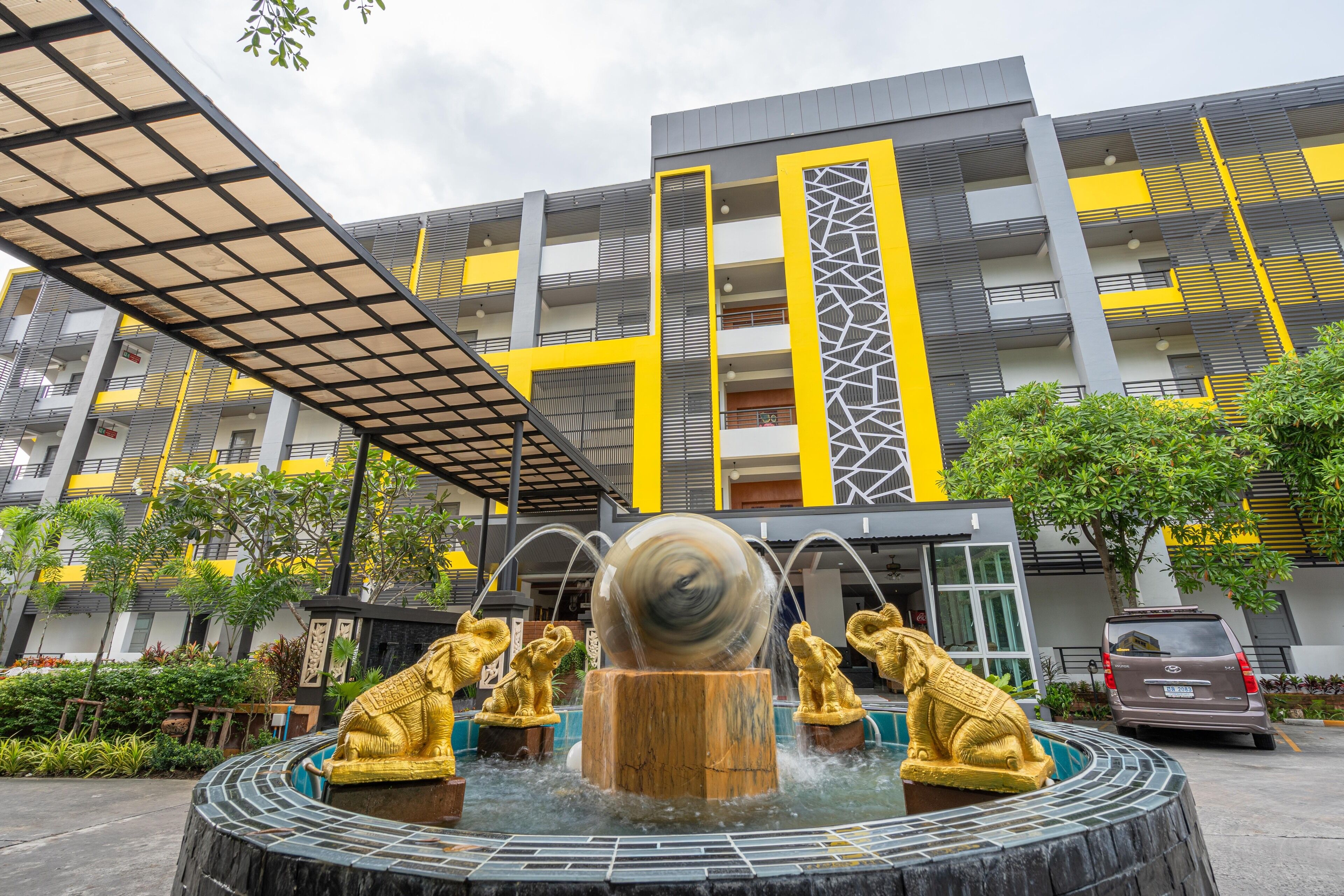A modern building with a courtyard featuring a water fountain with golden statues and a large spherical structure.