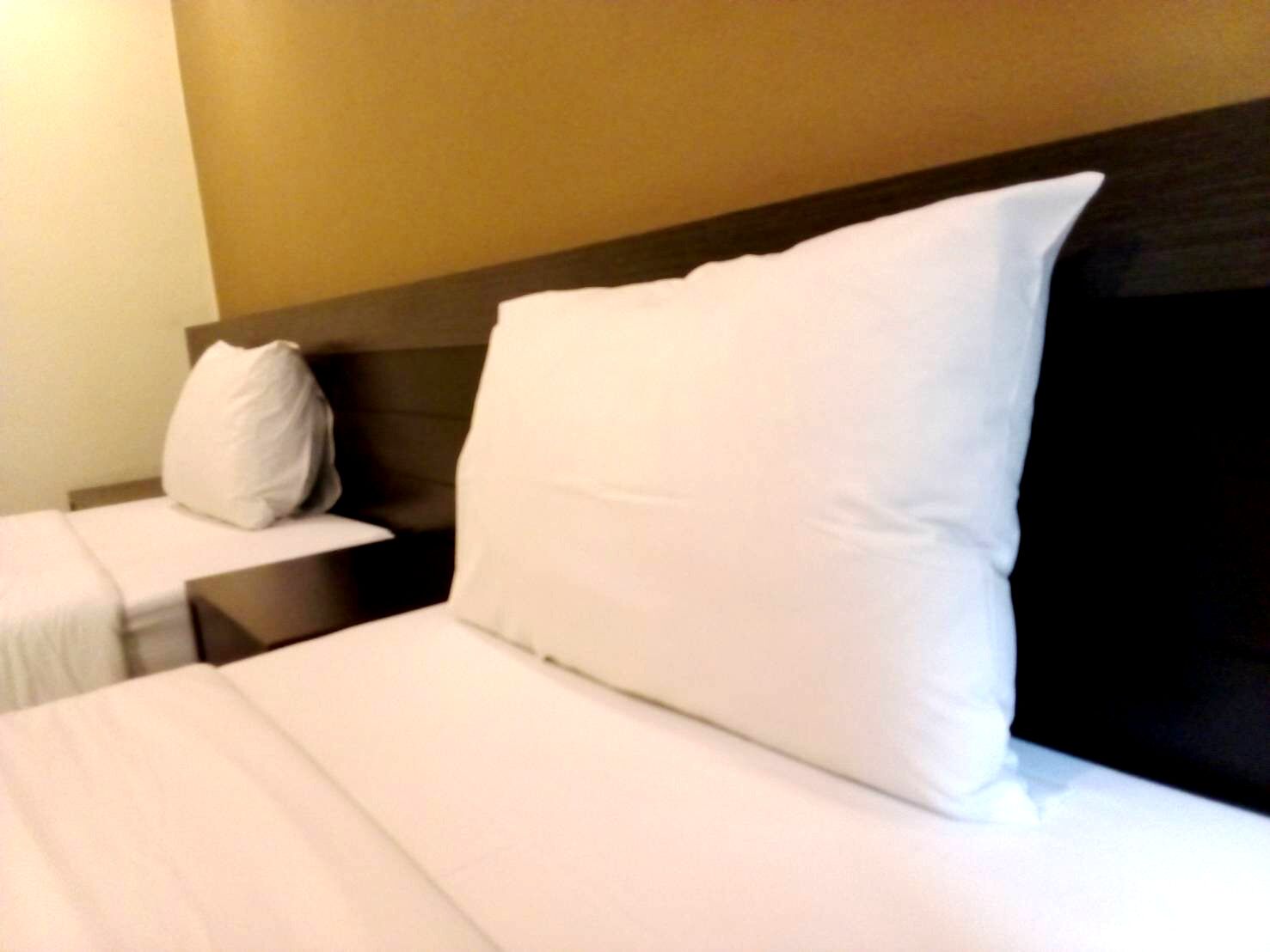 A hotel room with a bed, a nightstand, and a pillow.