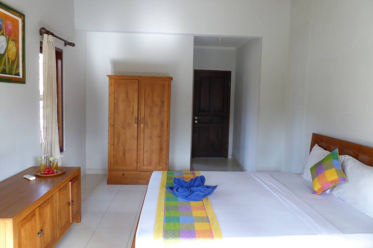 A bedroom with a wooden wardrobe, a bed with a colorful quilt, and a door leading to another room.