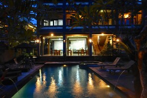 A pool area with lounge chairs and a building with an open entrance. - Wenara Bali Bungalow (Ubud)