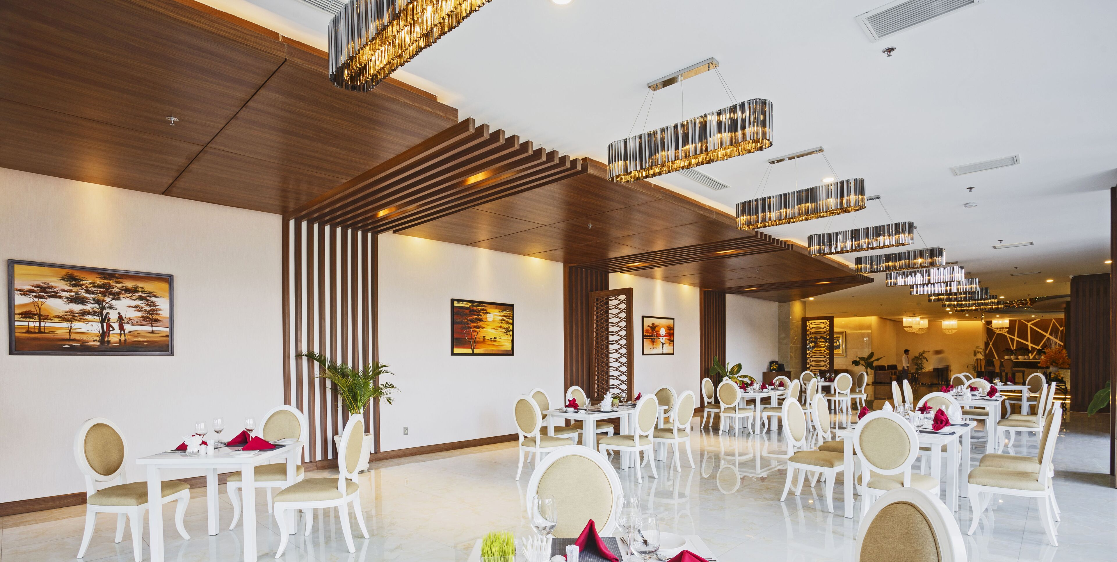A spacious dining area with white tables and chairs, wooden ceiling panels, and modern chandeliers.