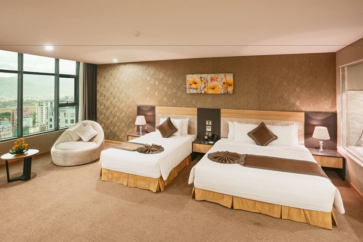 A hotel room with two beds, a round chair, a city view, and a painting on the wall.
