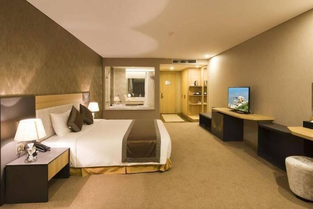A hotel room with a bed, bedside tables, a TV, a desk, and a bathroom visible through an open door.