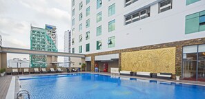 Et moderne hotel med swimmingpool, udendørs siddepladser og en stor dekorativ væg.