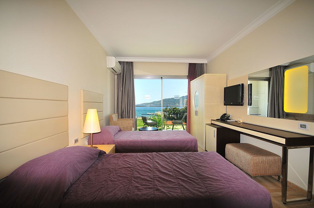 Ein Hotelzimmer mit zwei Betten, einem Schreibtisch, einem Sessel, einem Fernseher und Meerblick.