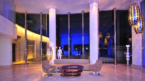 Een moderne lobby met een ronde zithoek, grote glazen deuren en een spiegelende kolom.