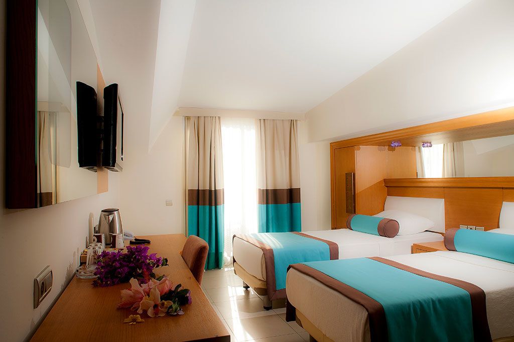 A hotel room with two beds, a wooden headboard, a desk with a coffee maker, and a mirror.